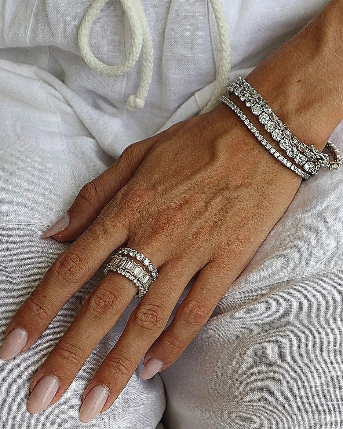 A hand wearing stone-set bracelets and stacked rings against white fabric