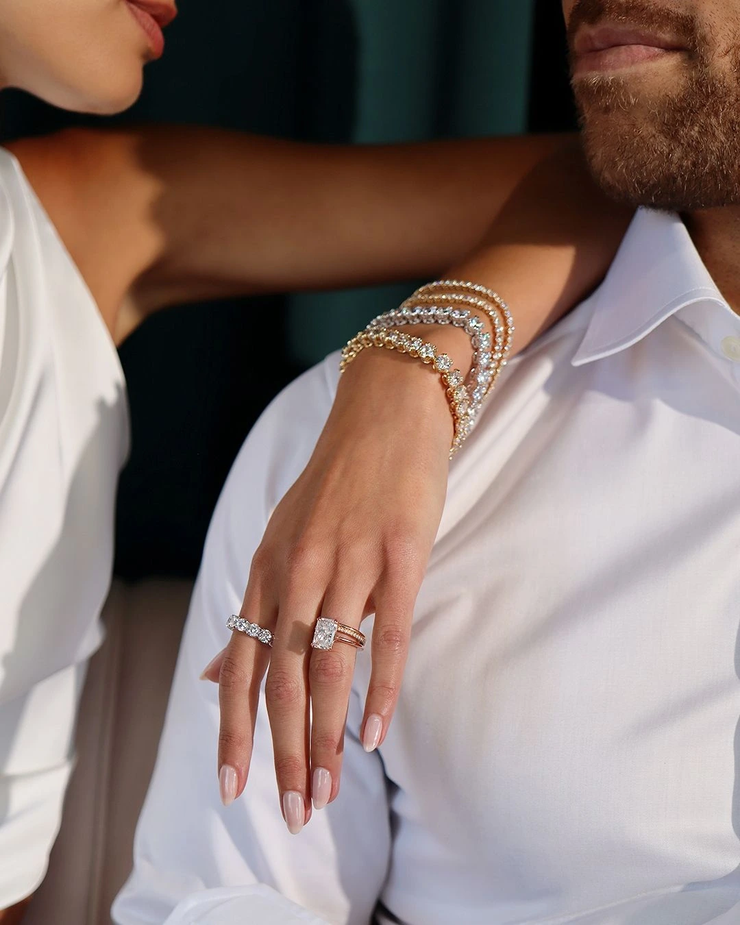 Stacked bracelets and stone-set rings worn against white clothing