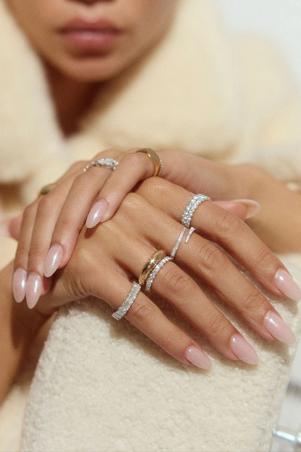 A woman wearing slim gold and white-metal rings on her hands against soft fabric