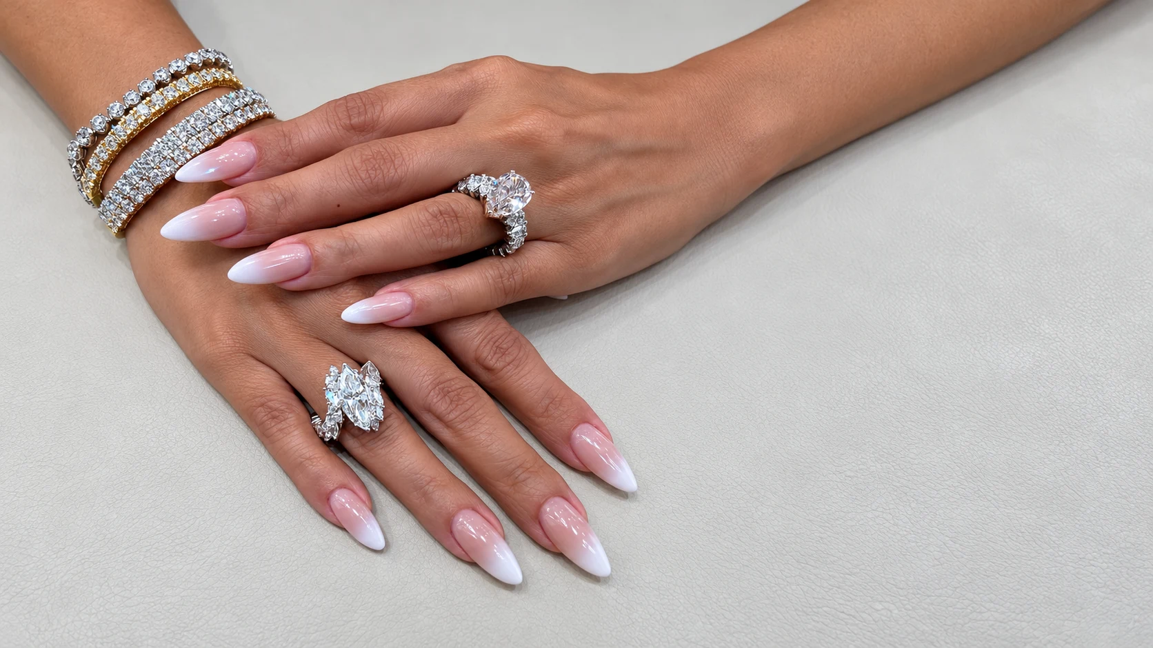 Overlapping hands wearing stacked bracelets and statement rings on a light textured surface